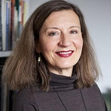white woman with shoulder length dark hair wearing a brown sweater in an office full of books