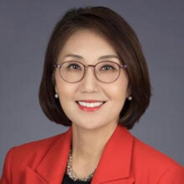 asian woman with glasses and short dark hair wearing a red blazer with a grey backdrop