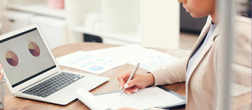 stock image of a woman writing on a notepad in front of a laptop
