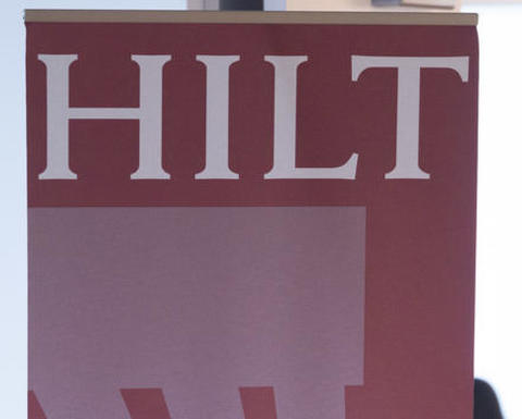 HILT vertical banner placed in a well lit room with a man in the background having lunch.